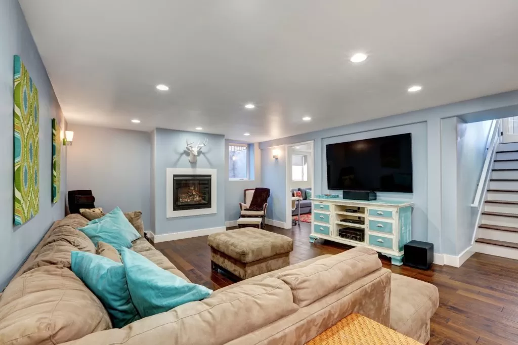 Pastel blue walls in basement living room interior. Large corner sofa with blue pillows and ottoman. Vintage white and blue TV cabinet. Northwest, USA