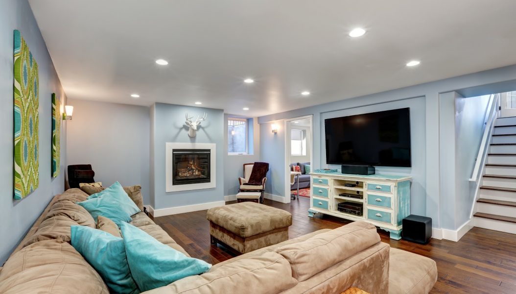 Pastel blue walls in basement living room interior. Large corner sofa with blue pillows and ottoman. Vintage white and blue TV cabinet. Northwest, USA